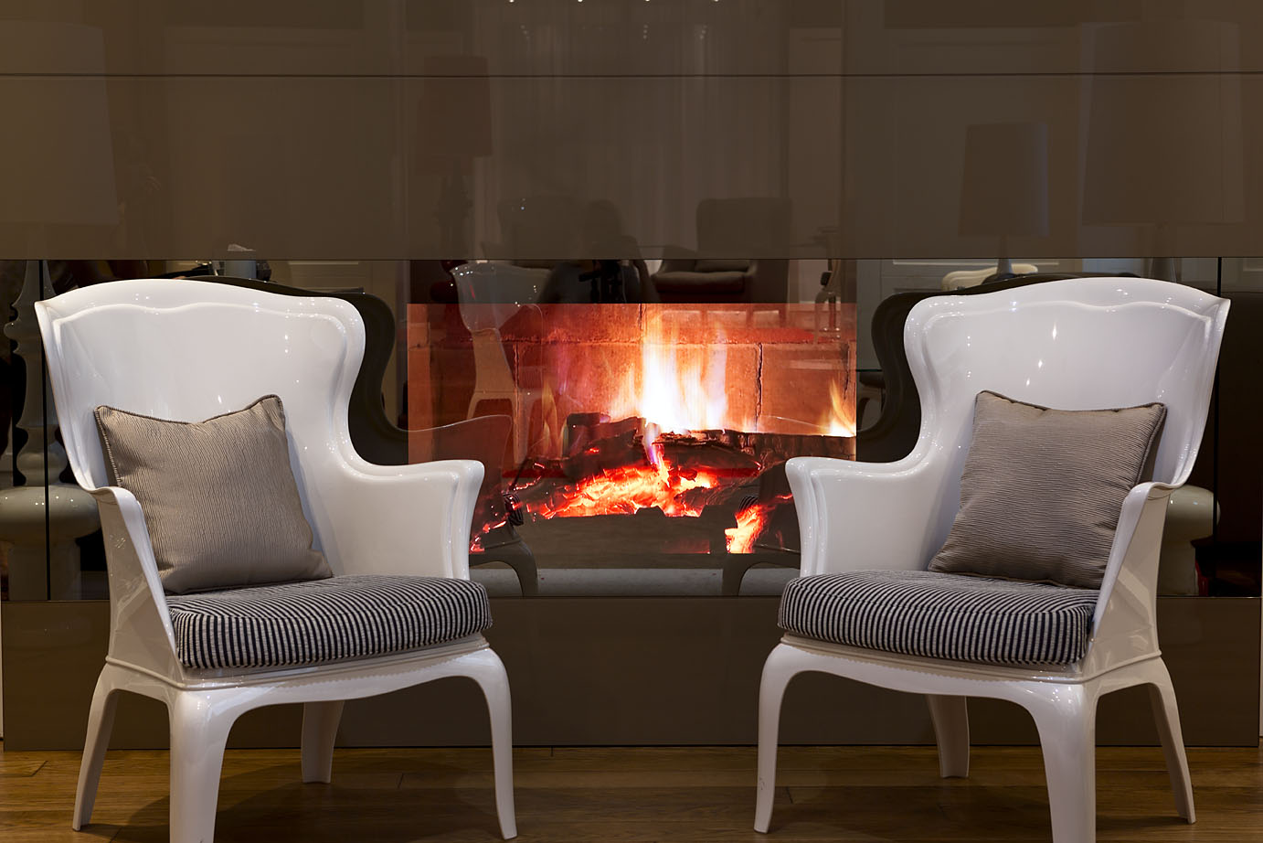 Zwei weiße Stühle mit Kissen stehen vor einem brennenden Holzkamin 