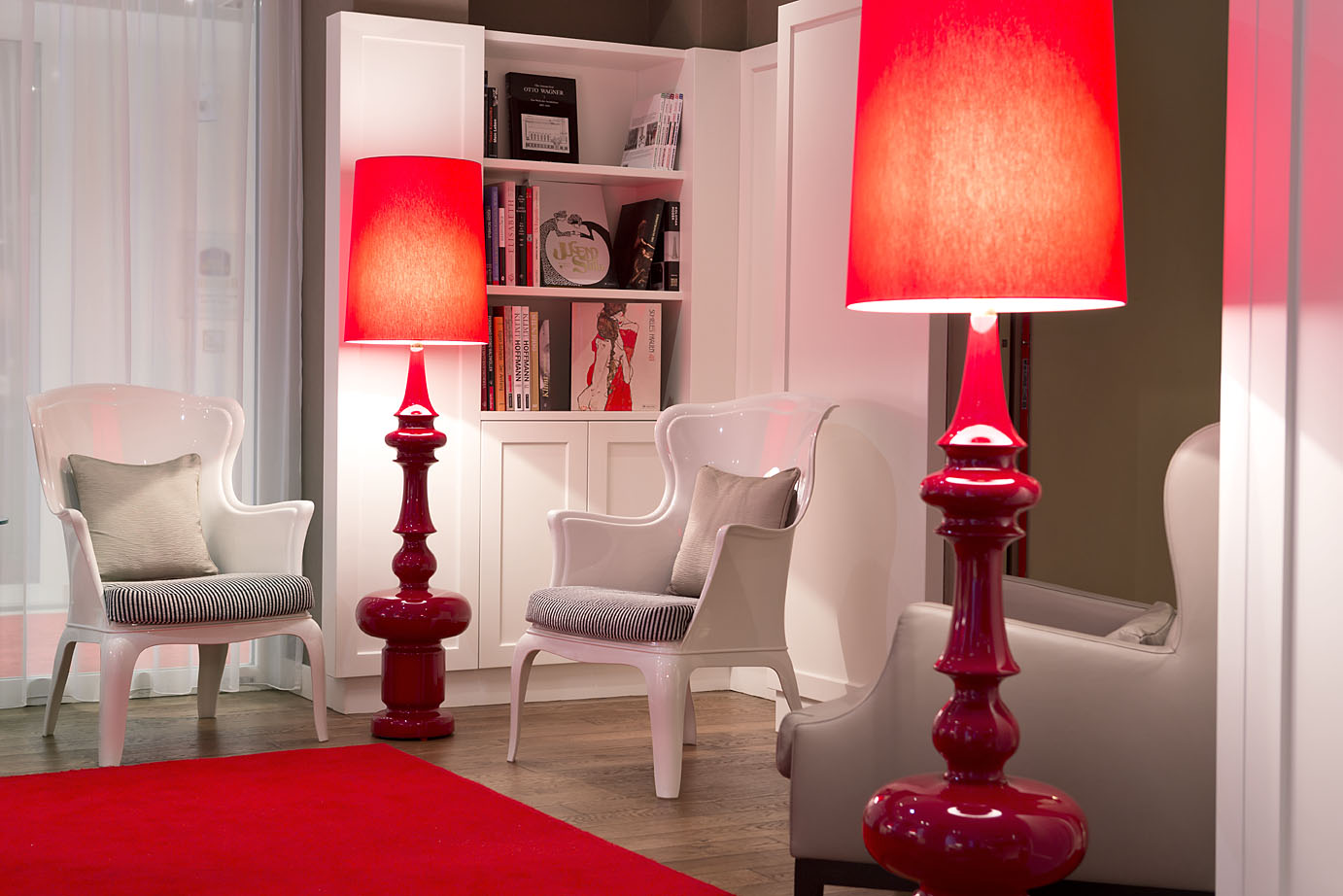 In der Bücherei des Hotels stehen zwei weiße Stühle und rote Stehlampen
