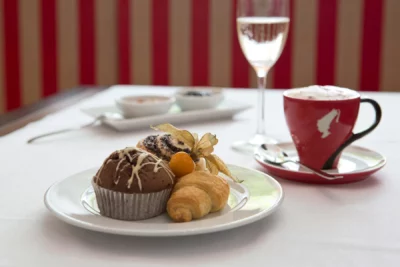 Teller mit Muffins und Obst, dazu ein Kaffee und ein Glas Sekt im Hotelrestaurant