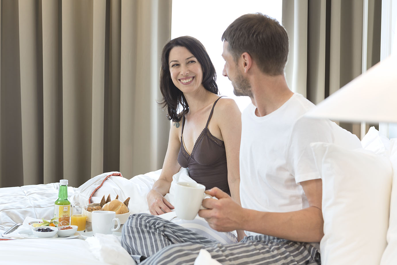 Ein Paar genießt das Frühstück mit Obst, Brötchen und Kaffee im Bett des Hotels in Wien