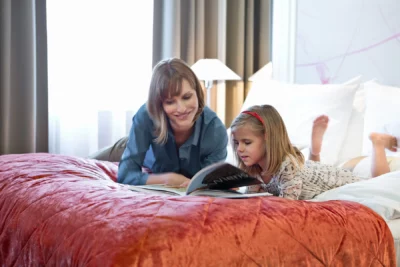 Eine Mutter und ihre Tochter liegen auf einem Doppelbett und lesen eine Zeitschrift