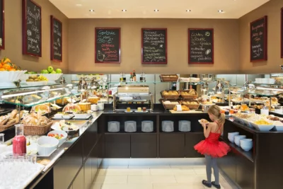 Ein Mädchen in rotem Kleid sucht sich am Hotelbuffet etwas zu Essen aus