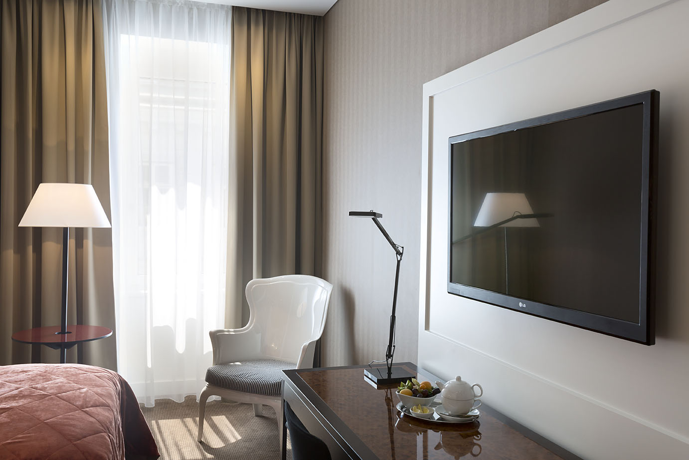 Doppelzimmer im Harmoniehotel mit Stehlampe, weißem Stuhl und großem Fernsehen