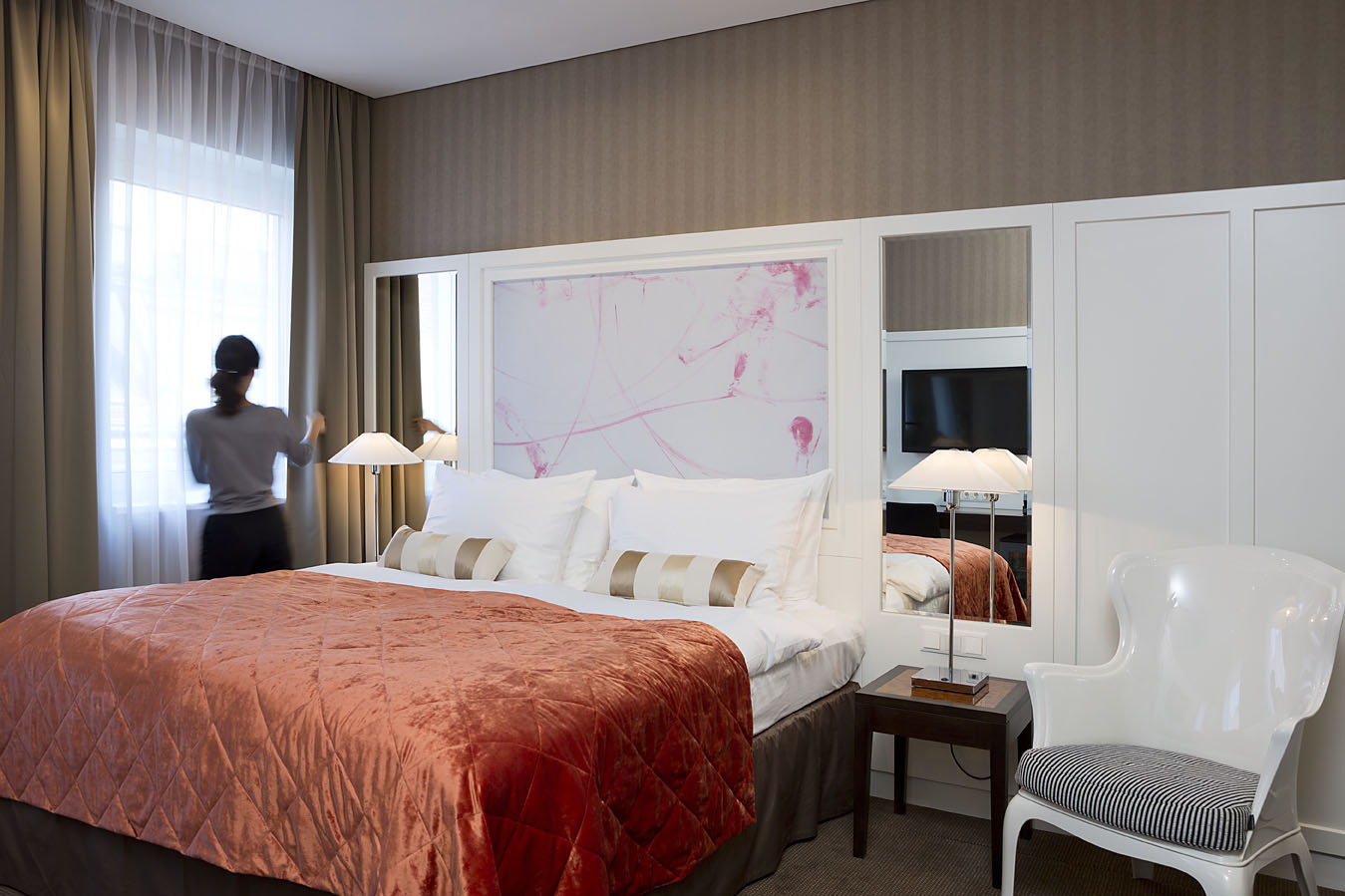 Eine Dame öffnet den beigen Vorhang in einem Zimmer des Harmonie Hotels Wien