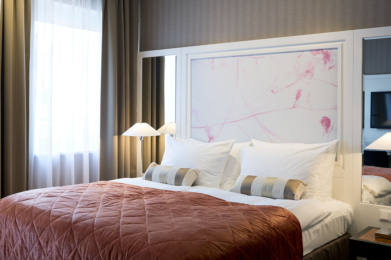 Doppelbett im Hotel in Wiens Zentrum mit roter Tagesdecke und Wandkunstwerk