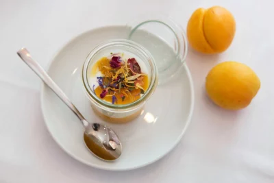 Auf einem Teller steht ein Weck Glas mit Jogurt und zwei Aprikosen