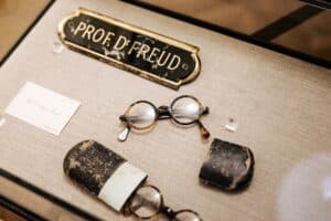 Detailaufnahme eines Namensschildes von Sigmund Freud liegend neben mehrere Brillen und einem Etui.
